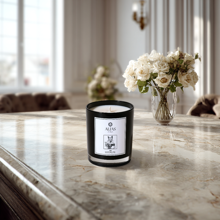 Candle with a label on a marble surface, surrounded by flowers in the background